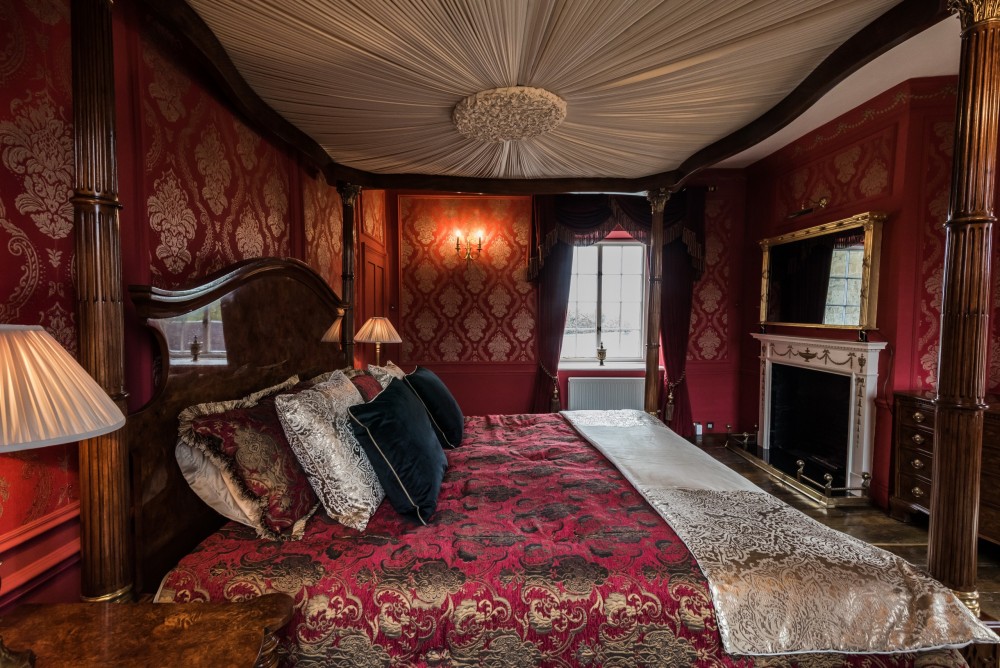 Commercial Interiors Photograph of red bedroom with a dark wood four poster bed